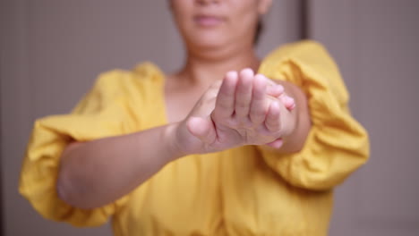una mujer con un vestido amarillo está estirando su brazo izquierdo mientras lo exprime y masajea suavemente hasta las puntas de los dedos