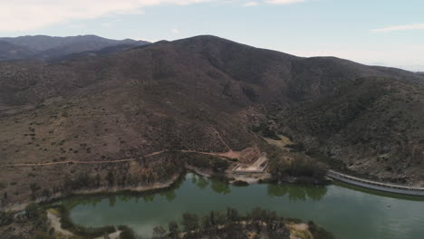 aerial: drone zoom in of mountain by green water lake