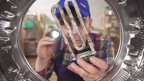 close up of a repairman holding a broken heating element next to the washing machine inside view