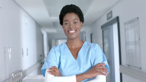 portrait of happy african american female doctor wearing scrubs, smiling in corridor, slow motion