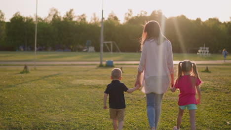 Mother-with-children-walk-joying-hands-along-field-in-park