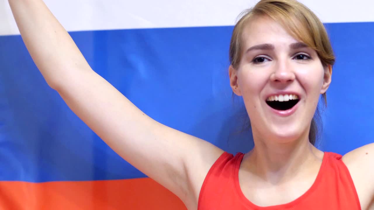 молодая русская женщина празднует, держа в руках флаг россии в замедленном движении.