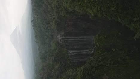 vertical format: stunning tumpak sewu waterfall with java volcano cone