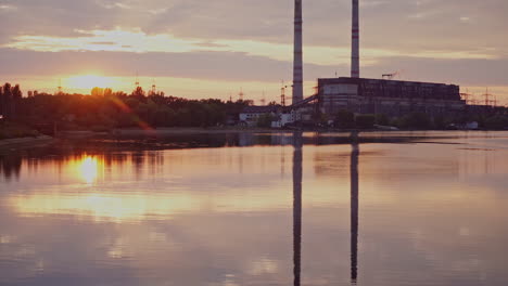 river at sunset on manufacturing background. industrial pipes reflect in the evening water. metallurgical plant near the river.