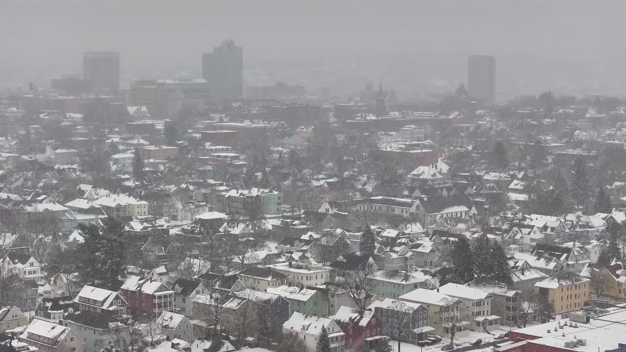 Worcester’s residential area extends toward the downtown skyline. Dense houses line the streets below. Overhead vantage reveals layered city blocks, aerial.