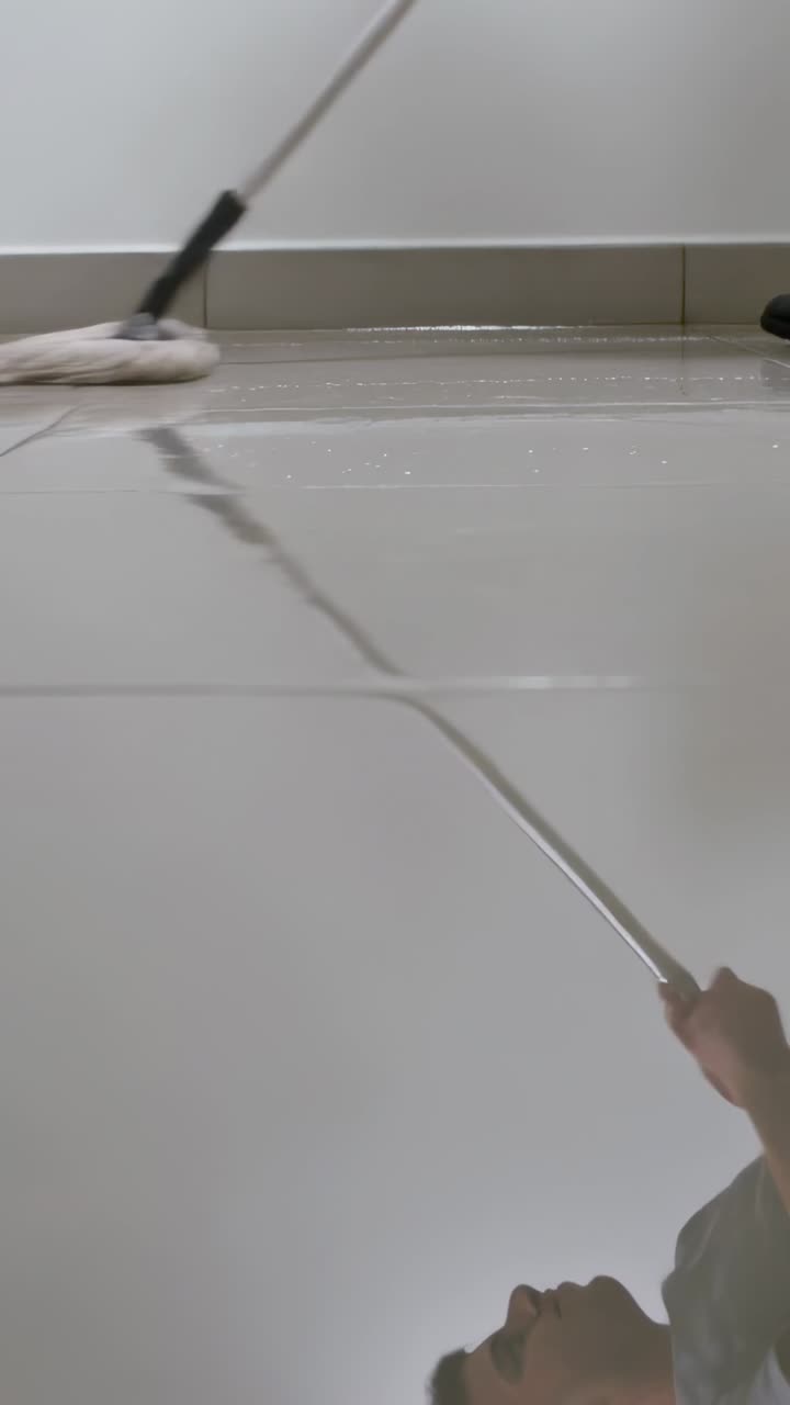 Vertical video: Mopping man in shirt moving mop after seeing reflection in corridor, cleaning tiles