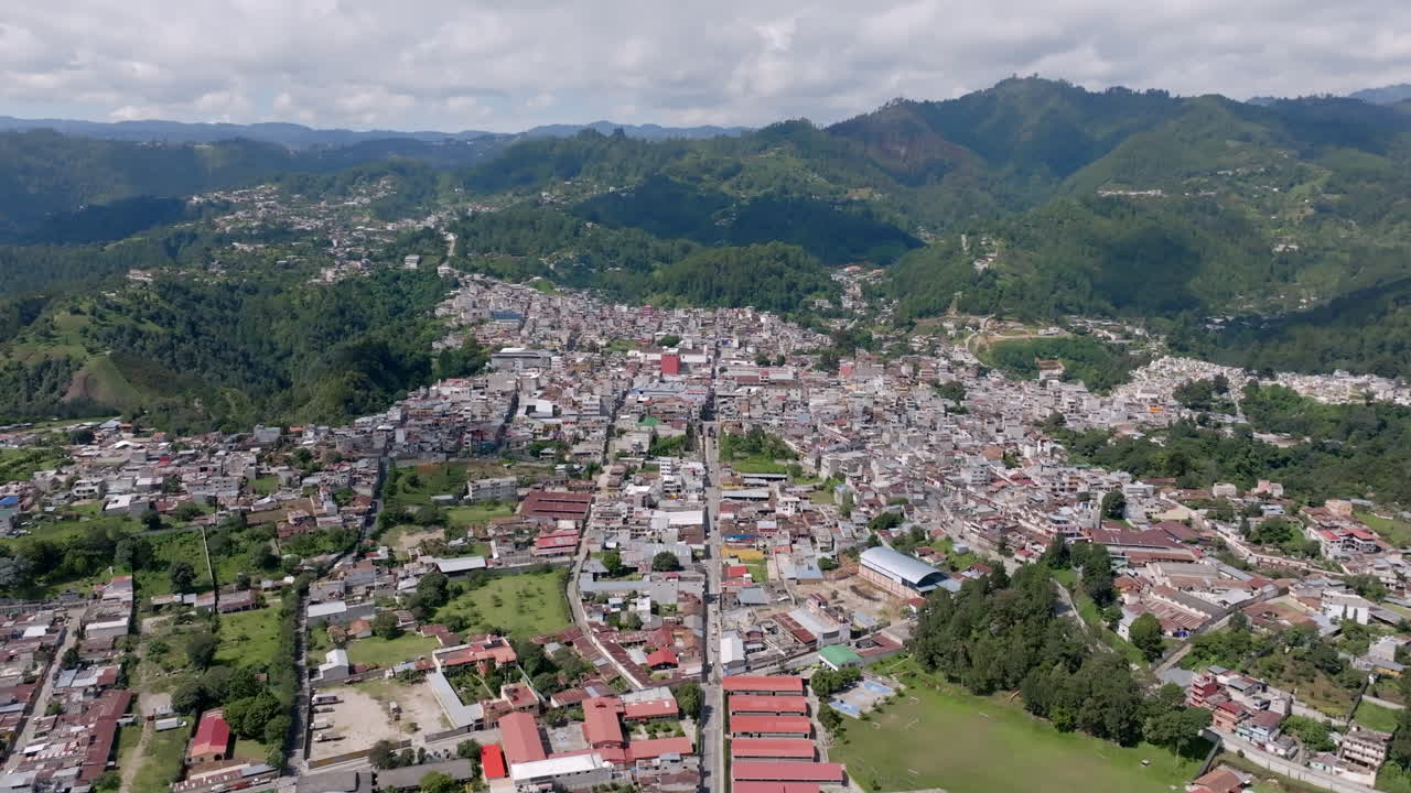Aerial video of Chichicastenango captures a dense town center with red rooftops and streets leading to surrounding mountains covered in rich green forests