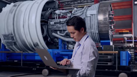 side view of an asian male professional worker standing with his laptop with airplane engine maintenance conducted, analytics checking the turbine, typing on his laptop's keybaord with meditation