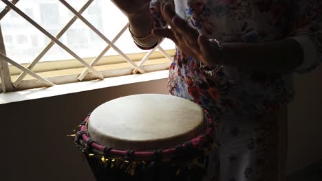 medium wide looking down isolated shot of a woman playing djembe drum by the side of a window