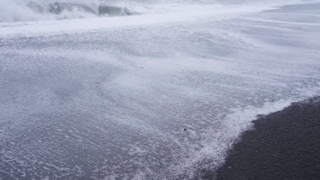 Foamy-water-rushing-over-black-sand-on-a-beach-in-Iceland---Slow-motion