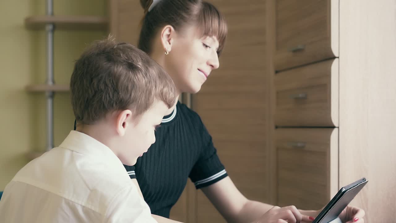 una joven madre bonita le muestra a su hijo cómo hacer la tarea usando una tableta.