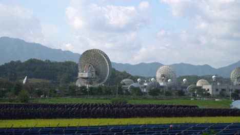 kt sat satellite center in geumsan, south korea at daytime - zoom-in shot through rice field and ginseng fields toward dishes