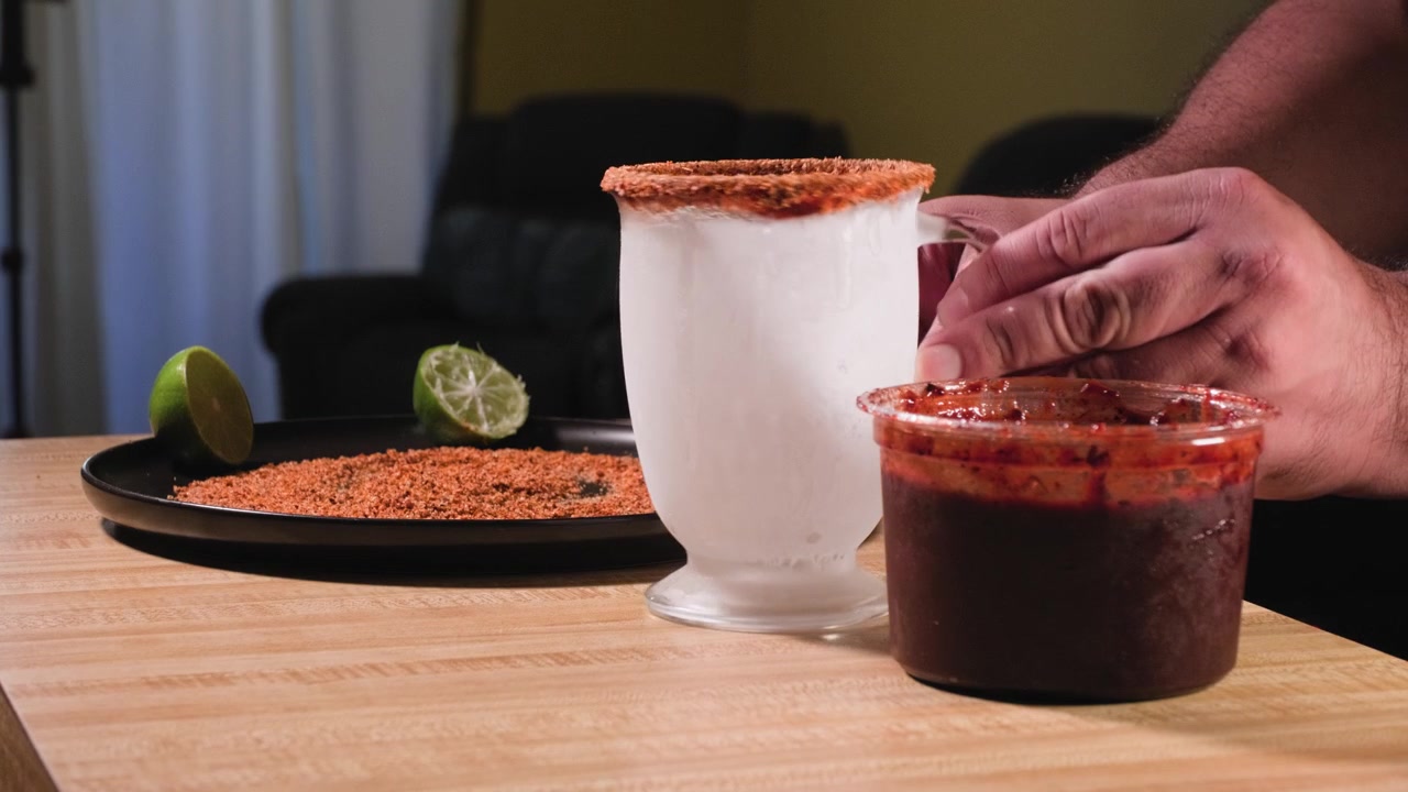 Filmato ravvicinato di un uomo che ricopre il bordo di un bicchiere ghiacciato con condimento Tajin mentre prepara una bevanda chamoy fatta in casa.