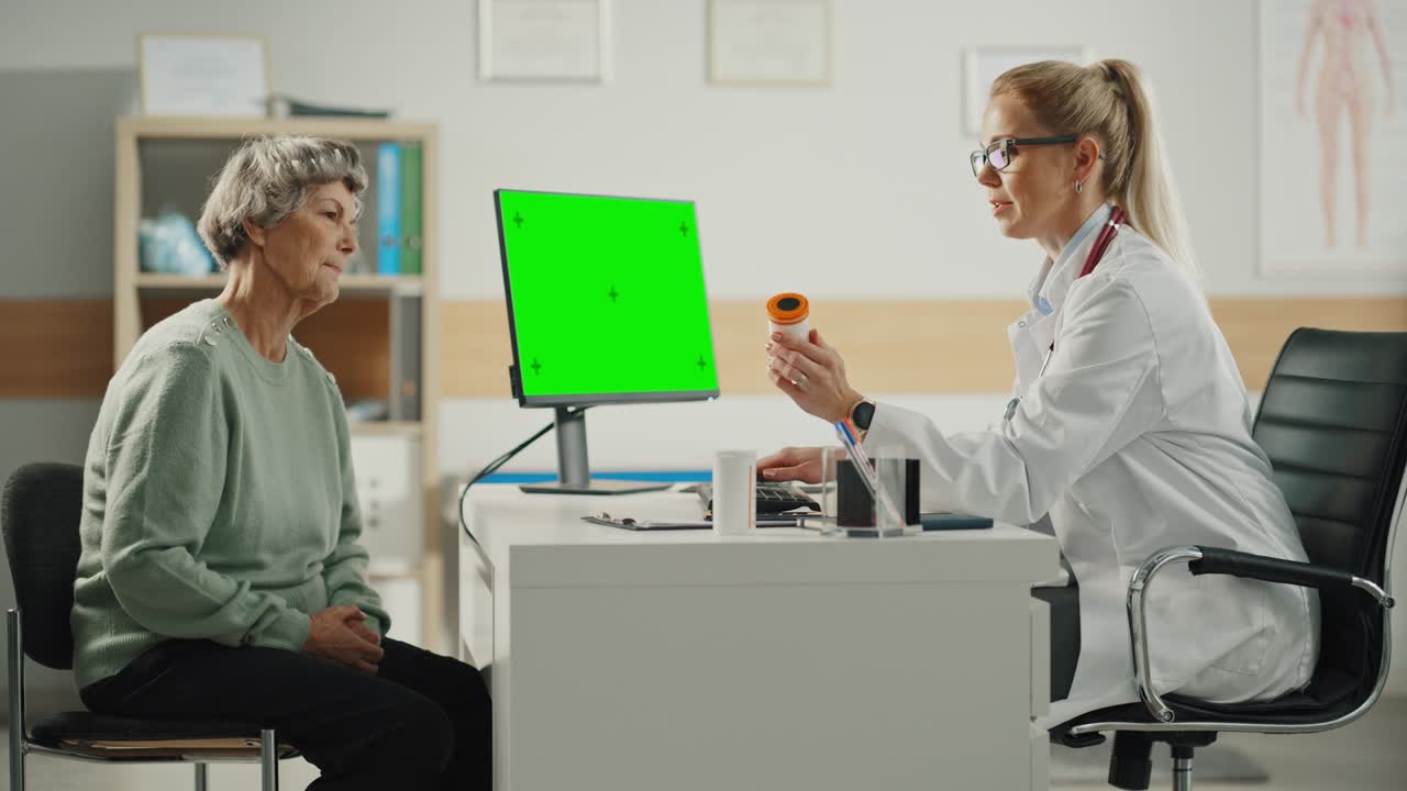 여성 가족 의사는 녹색 화면 디스플레이를 가진 컴퓨터를 사용하고 건강 클리닉에서 상담하는 동안 고령 환자와 이야기하고 있습니다.