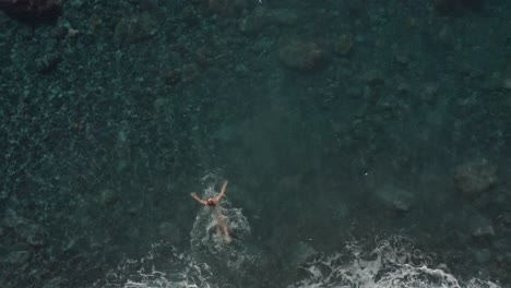 fit woman in bikini on summer holiday walking into clear water, jumping in, going for a swim, top down aerial