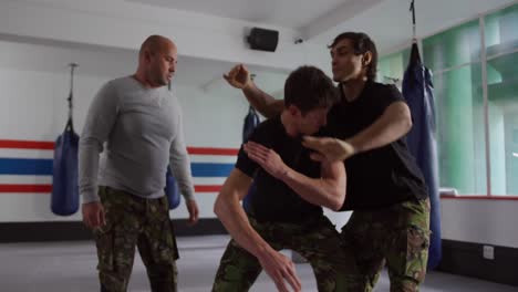 dos hombres caucásicos aprendiendo autodefensa de un entrenador en el gimnasio