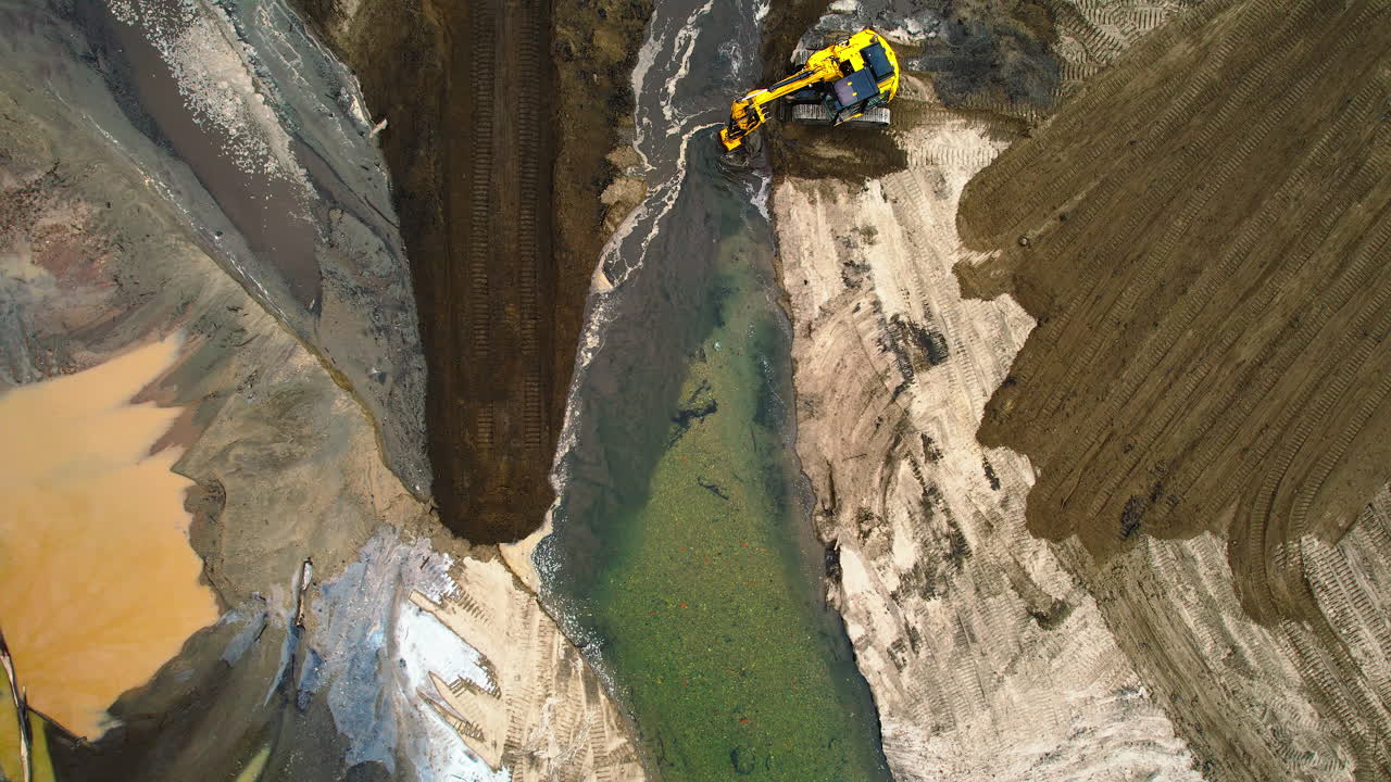 una excavadora que maneja sedimentos en un estanque de secado, rodeada de altas paredes de tierra, vista aérea