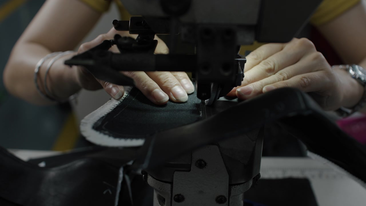 Worker sewing shoe material with industrial machine in a footwear production setting