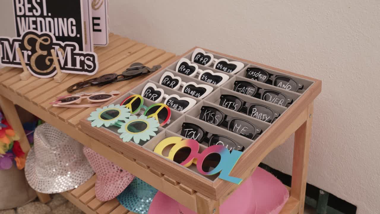 Assorted party sunglasses with fun designs and signs on a wooden table indoors