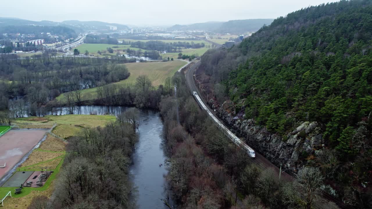 Drone shot of a train traveling along a winding hilly railway through rural Gothenburg, Sweden, captured on a misty morning landscape