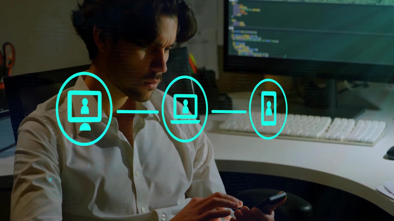 IT developer rubbing forehead at office desk, showing neon desktop laptop smartphone icons