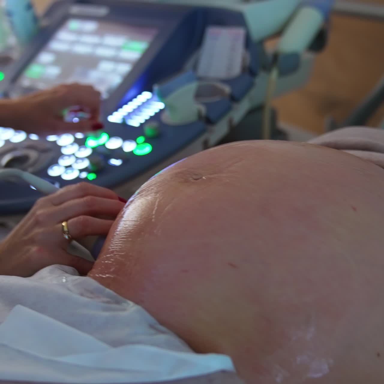 Moderna macchina a ultrasuoni con diversi pulsanti luminosi. Medico che preme rapidamente i tasti sull'apparecchio mentre muove il dispositivo nell'altra mano sul ventre di una donna incinta