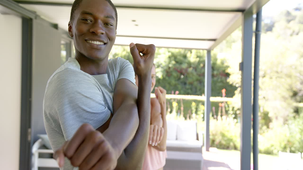 Uomo afroamericano sorridente che si stira le braccia con una donna sullo sfondo vicino al patio a bordo piscina, con spazio per il testo.