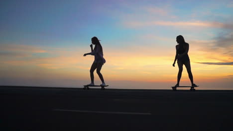 as the sun sets, two friends skateboard on a road with mountains and a beautiful sky in the background, all captured in slow motion. they sport shorts