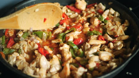 close up of wooden spoon mixing chicken fajitas ingredients cooking in pan