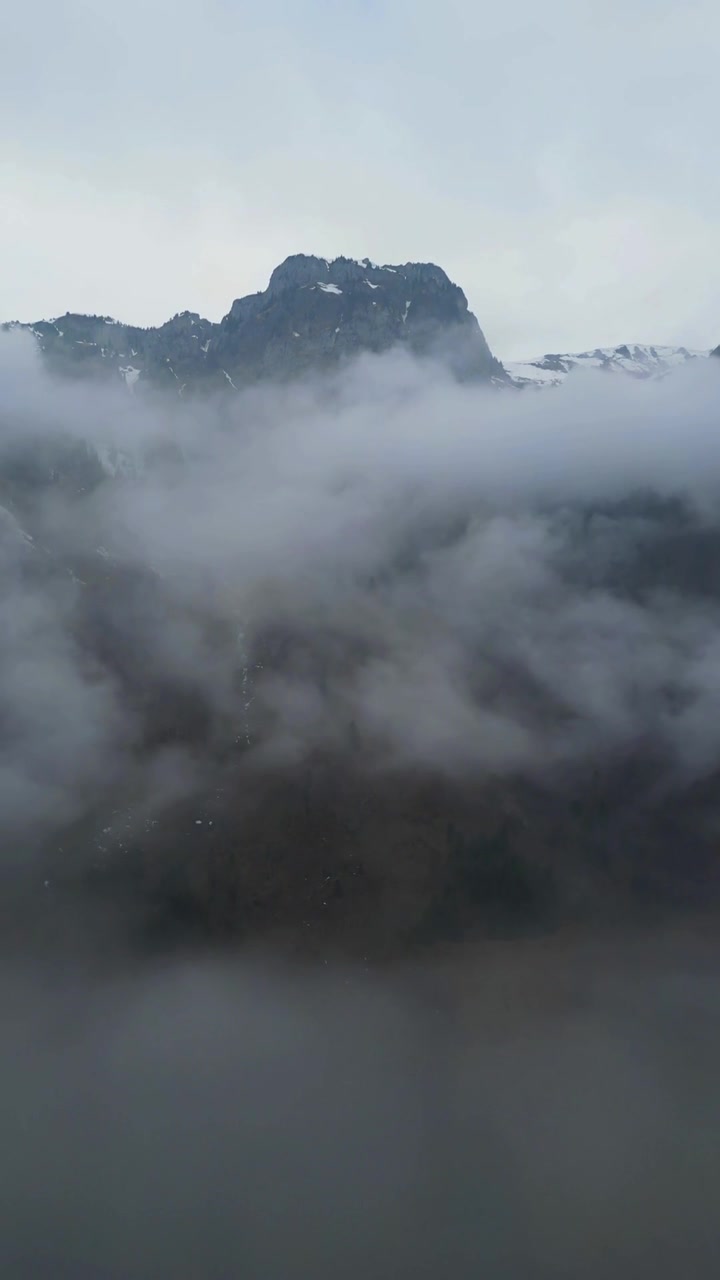 Paesaggio montuoso delle Alpi Svizzere avvolto in una fitta nebbia e nuvole basse, reel video verticale