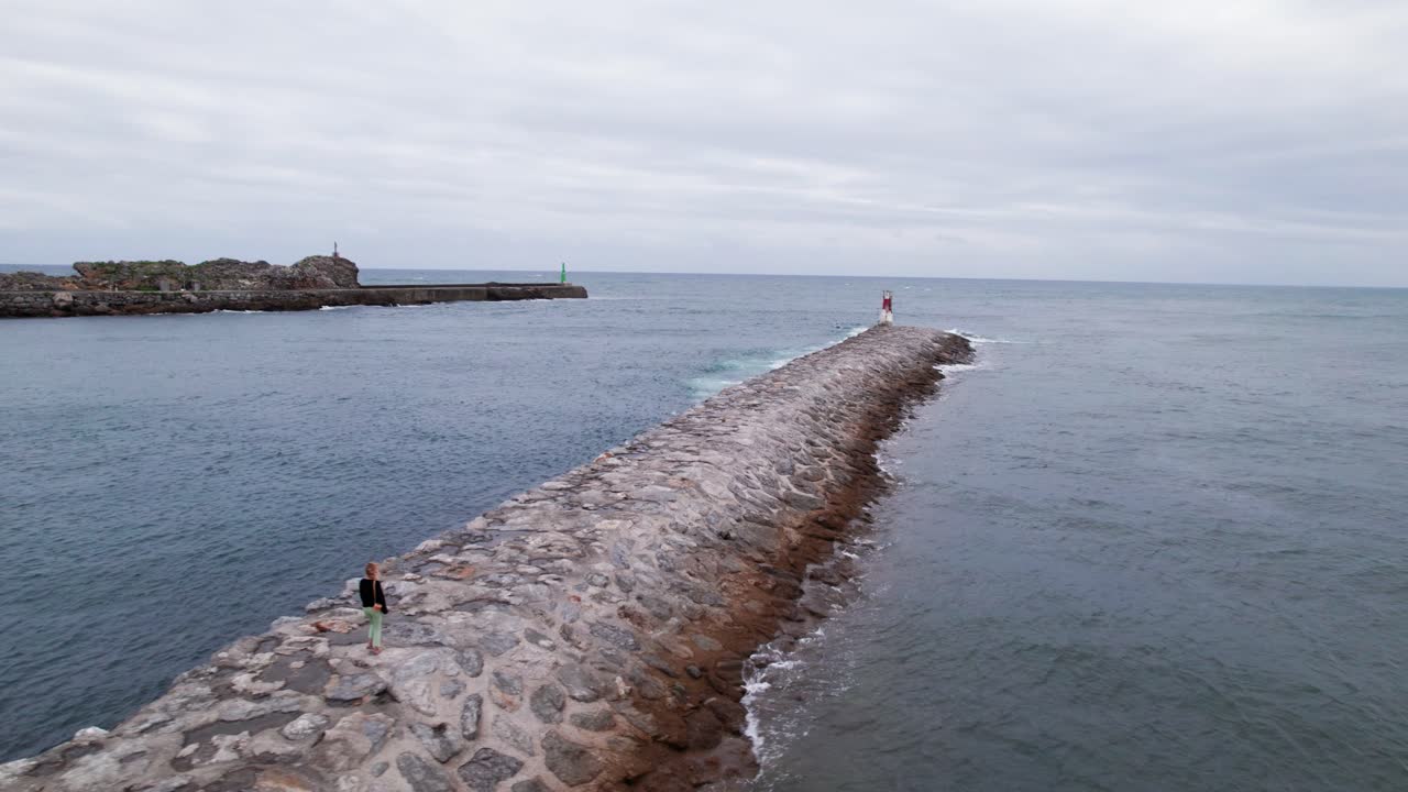 산 비센테 데 라 바르케라의 플라야 메론 해변에서 바위를 따라 걷는 여성의 공중 드론 샷