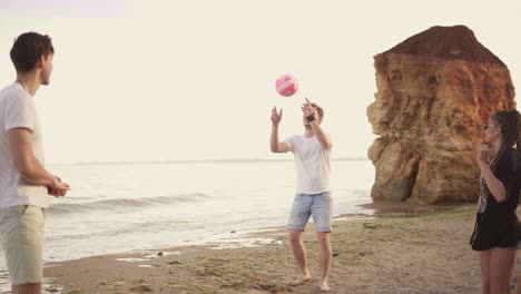 Jóvenes-Amigos-Alegres-Jugando-Voleibol-En-La-Playa-Junto-Al-Mar-Durante-La-Puesta-De-Sol.-Trabajo-En-Equipo.-Filmado-En-4k