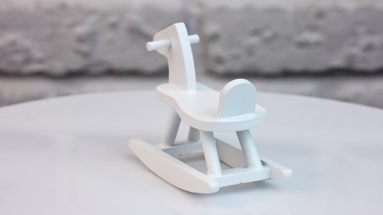 Small wooden rocking horse on a rotating table. Toy rocking horse for a doll's house. Tiny toy painted white. Close up.