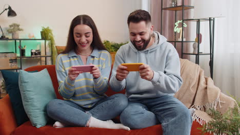 Familia-Feliz-Pareja-Casada-Hombre-Mujer-Jugando-Juegos-De-Aplicaciones-De-Video-Shooter-En-Línea-En-El-Teléfono-Inteligente-En-Casa