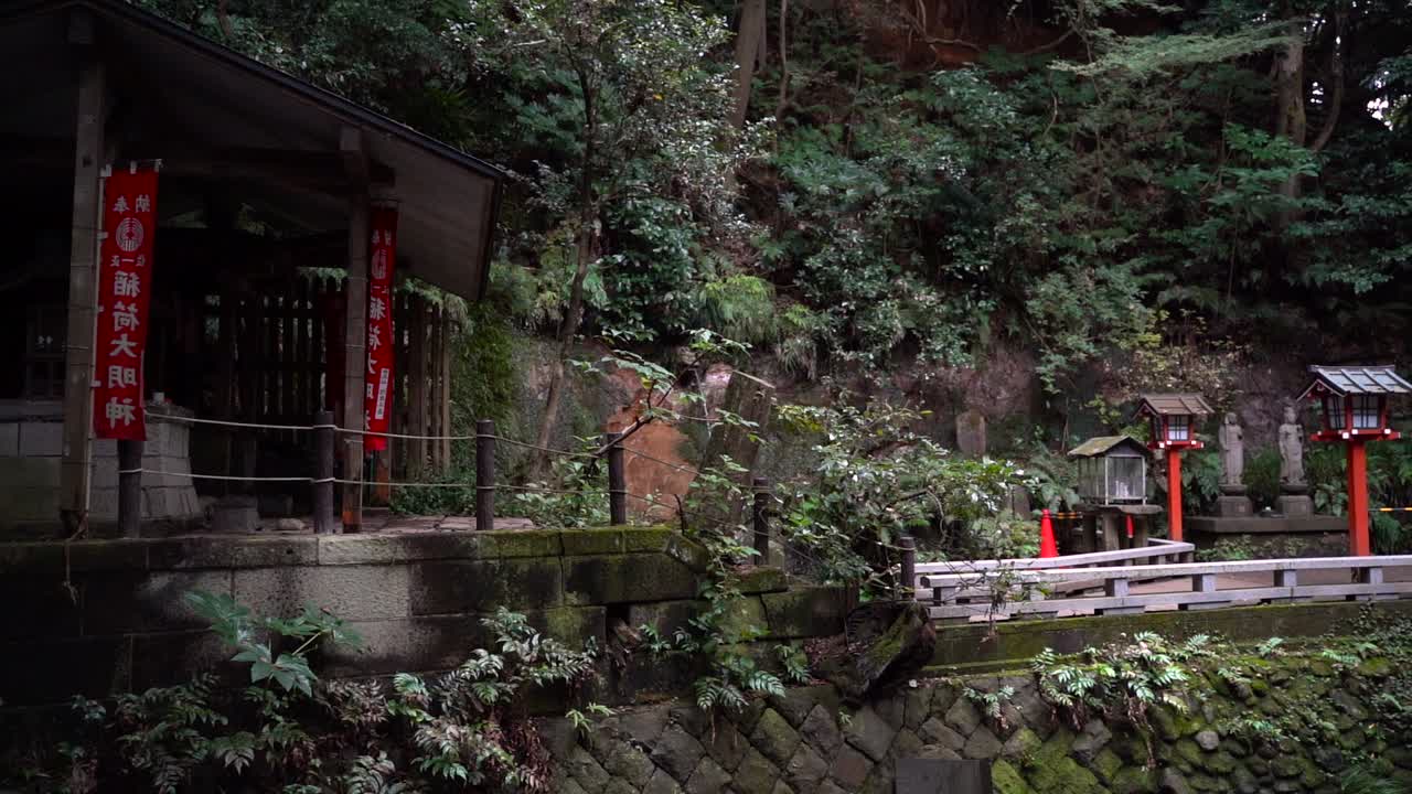 Slow pan across small Japanese temple inside forest with typical stone pillars and buildings - Slow Motion Shot