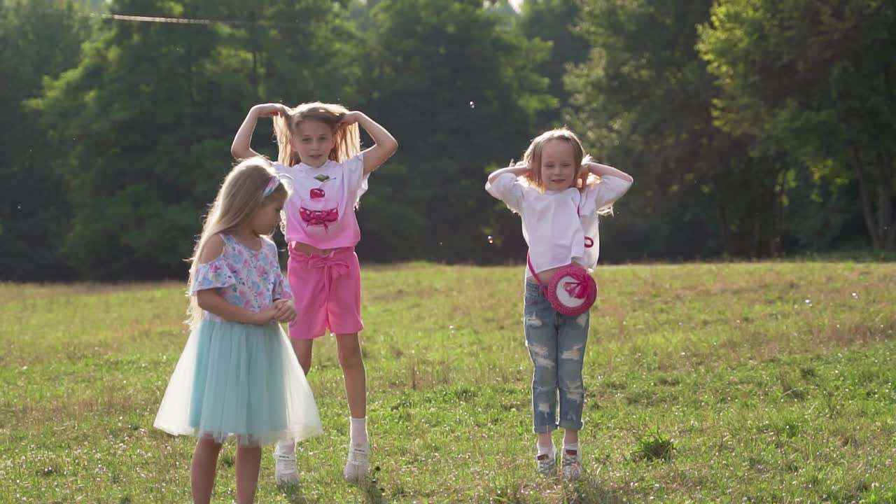 Little cute girls dance and jump in the park on the grass. The flowing hair of children. Slow motion