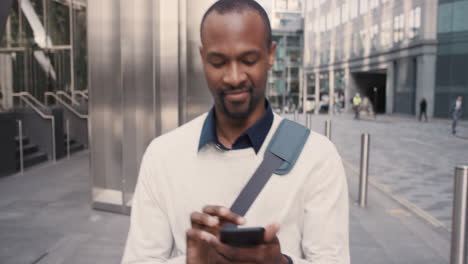 african american businessman walking through city using smart phone