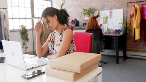 Thoughtful-biracial-female-fashion-designer-using-laptop-at-desk-in-studio,-slow-motion