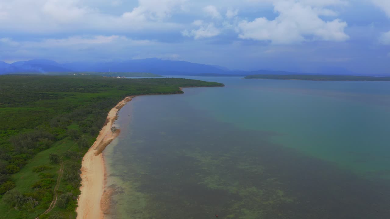 imágenes de drones que vuelan sobre la impresionante costa de nueva caledonia, mostrando una amplia y hermosa playa durante un día nublado
