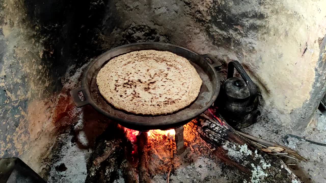 primer plano de cocinar pan en una sartén de hierro fundido descansando sobre trivets, sobre un fuego de madera de roble en una gran chimenea de piedra en una cocina tradicional