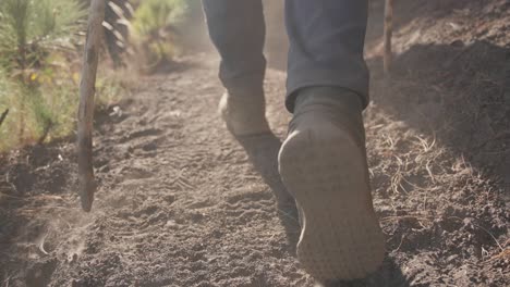 Slow-motion-follow-cam-captures-walking-hiker's-boots-on-the-dusty-trail,-backlit-cinematic-scene-with-golden-light