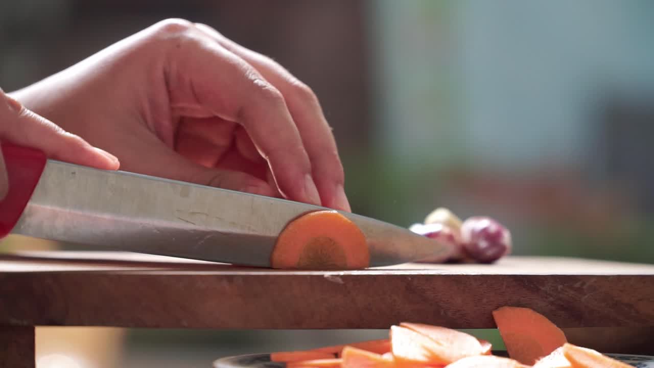 Macro view of hands carefully cutting the carrot with a stainless steel knife. Great for culinary, recipe, or healthy food content.