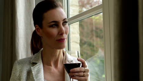 adult woman stands besides window drinking glass of red wine close up