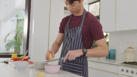 Asian-male-teenager-preparing-food-and-wearing-apron-in-kitchen