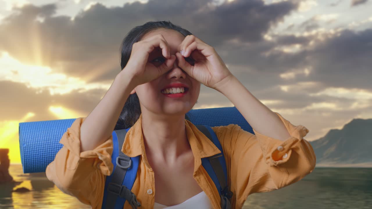 Close Up Of Asian Female Hiker With Mountaineering Backpack Making Binoculars Gesture Looking At Something Then Saying Wow While Standing on Beach During Sunset Time