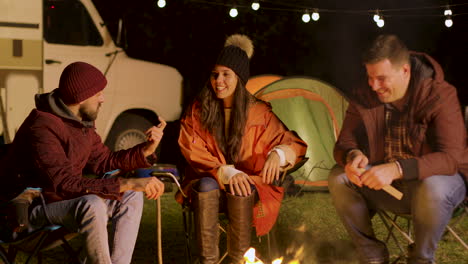 group of close friend relaxing together around camp fire in a cold night of autumn