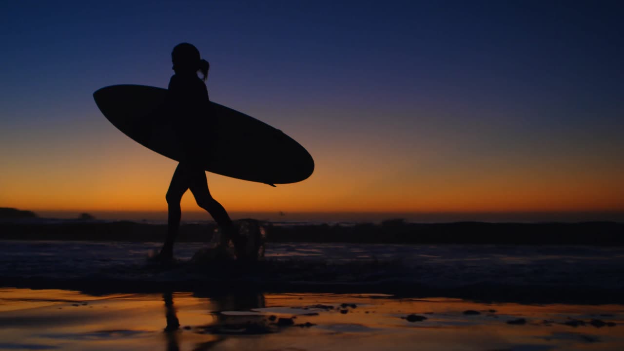 Surfista donna che cammina con la tavola da surf sulla spiaggia 4k