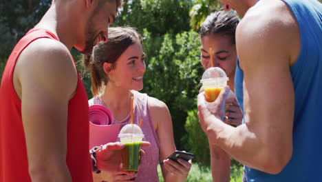 Fröhliche,-Vielfältige-Gruppe-Von-Männern-Und-Frauen,-Die-Nach-Dem-Yoga-Kurs-Im-Sonnigen-Park-Smartphones-Benutzen-Und-Sich-Unterhalten