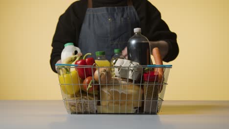 Studio-Shot-Of-Shop-Worker-Checking-Basic-Food-Items-In-Supermarket-Wire-Shopping-Basket-2