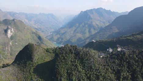 Drone-moves-over-rocky-mountain-top-reveal-a-small-village-and-green-Nho-Que-river-at-the-back-ground-Ha-Giang-Viet-Nam